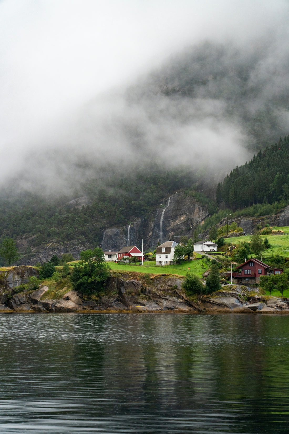 Small village nestled by a misty fjord with waterfalls.