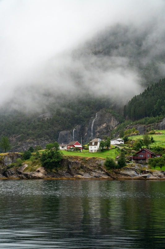 Small village nestled by a misty fjord with waterfalls.